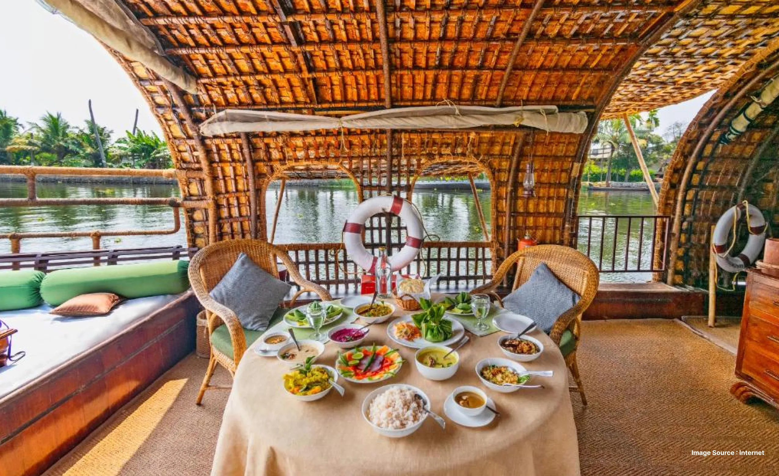 Traditional Kerala houseboat interior with a dining table set with local dishes, wicker chairs, and a view of calm backwaters through wooden windows