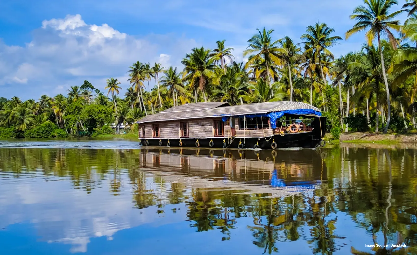 A traditional Kerala houseboat with palm trees during a clear Sunny day