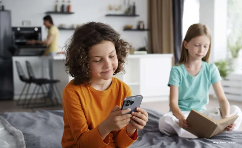 a child looking at his phone while another in the background reads a book