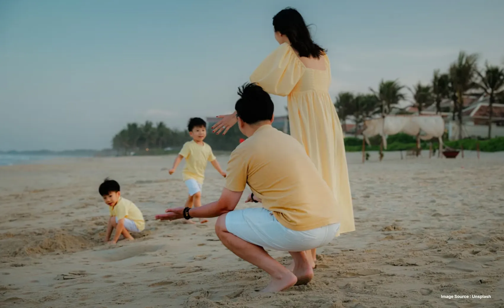 a family dressed in yellow and white playing with their two kids on the beach