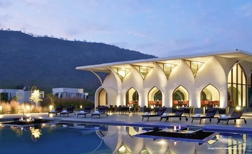 Modern luxury resort with illuminated poolside lounge and mountain backdrop at dusk.