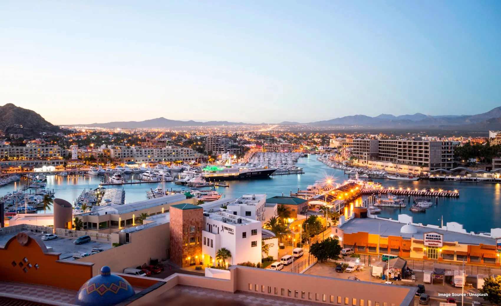aerial shot of cabo san lucas during sunset with lit up buildings and rooftops and beautiful waters