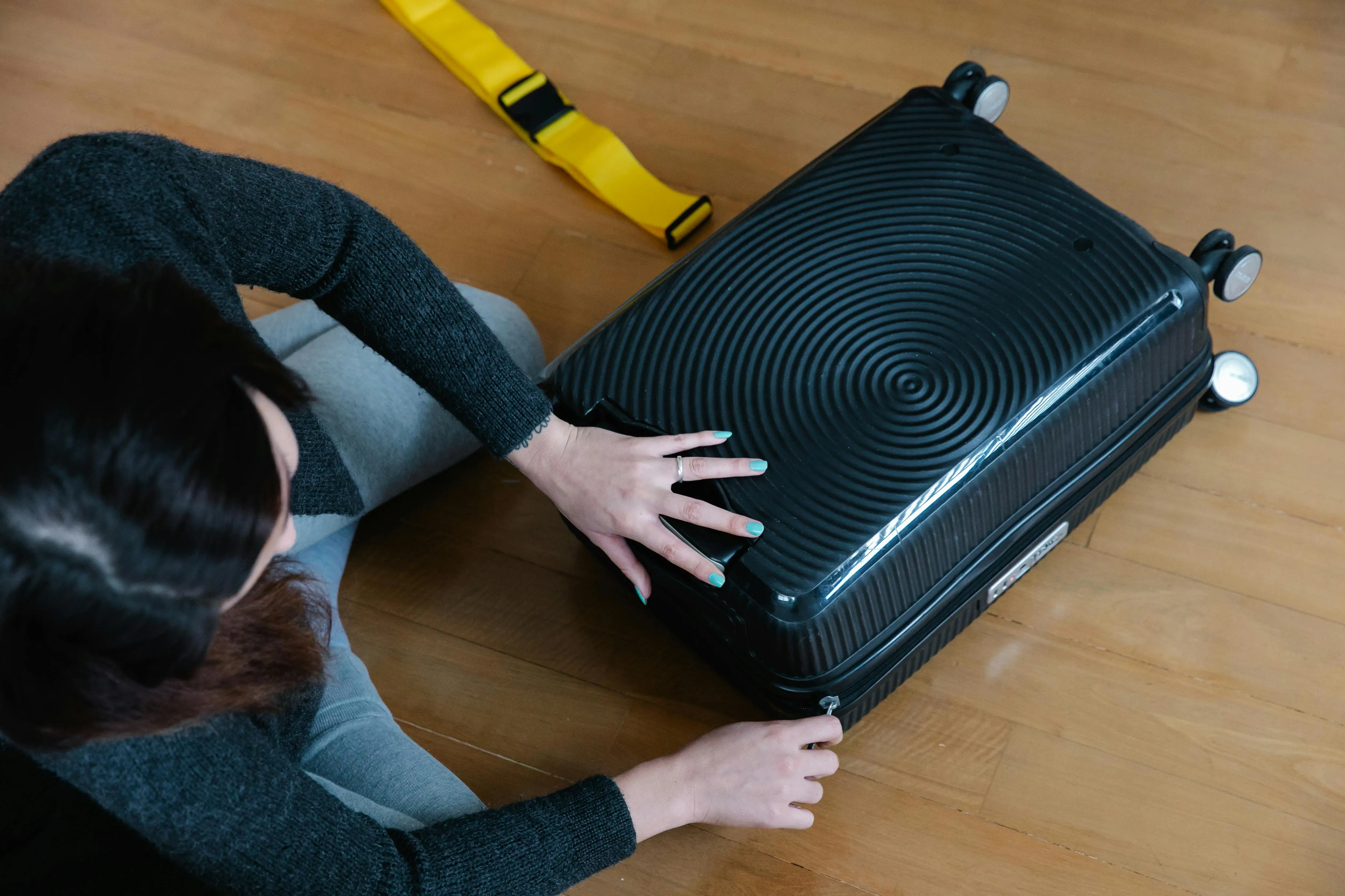 a women sitting on floor and trying to close her luggage