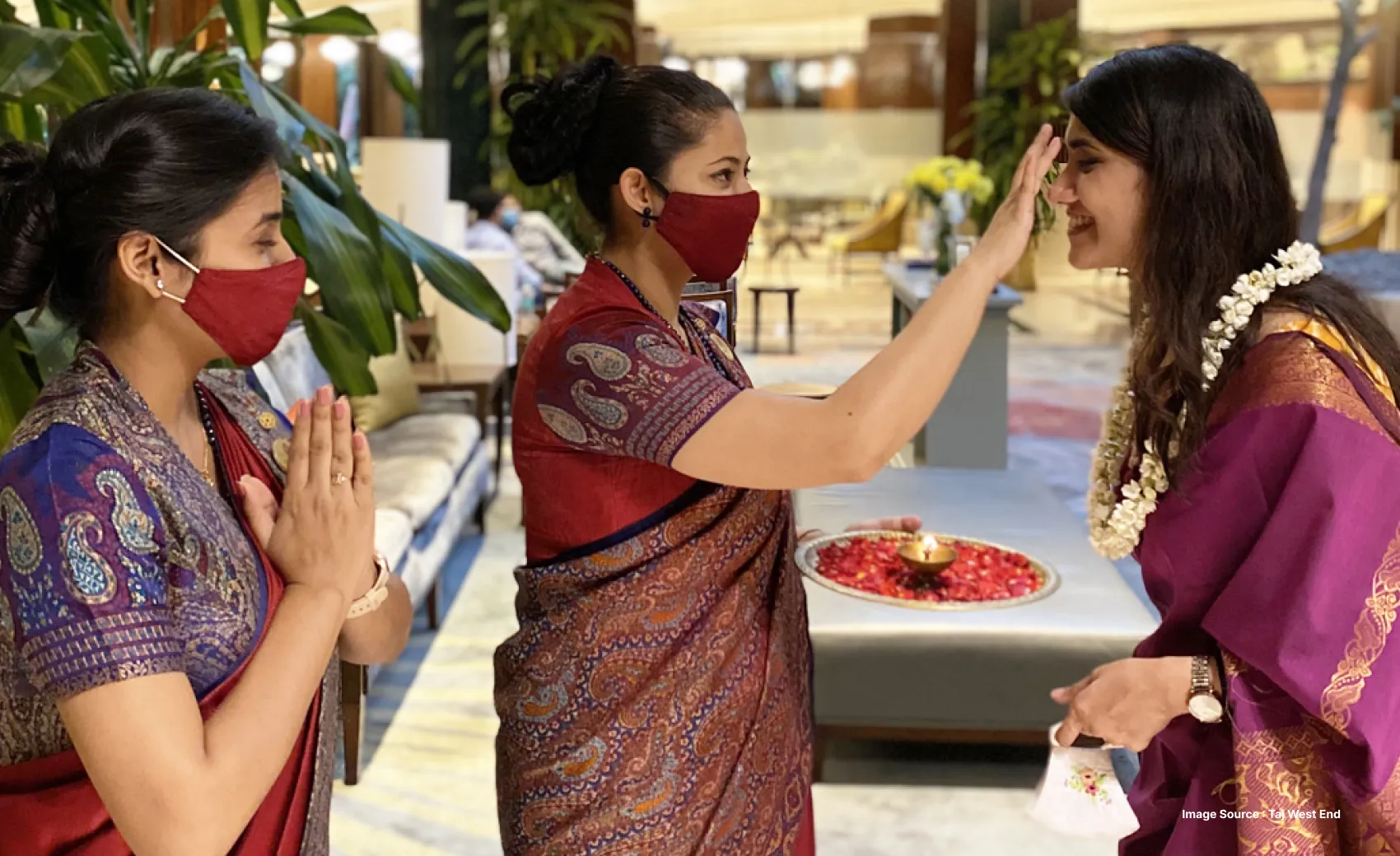 indian hotel staff, women dressed in sarees and wearing masks, welcoming a guest with tilak and namaste