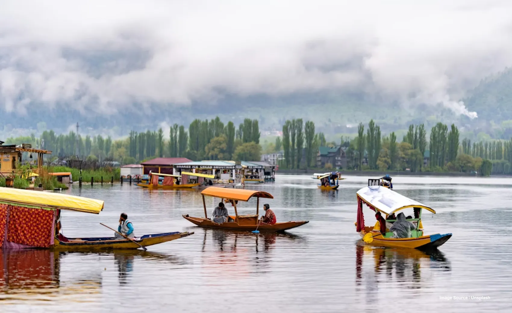 many colorful shikara boats cruising on the dal lake with tourists with the mountains with lush green trees in the backdrop
