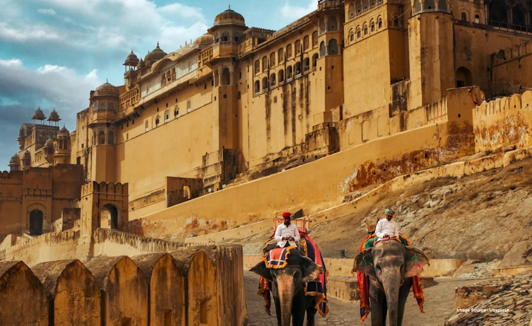 two decorated elephants with their caretakers sat on their back, walking down the walkway of the grand amer fort in rajasthan