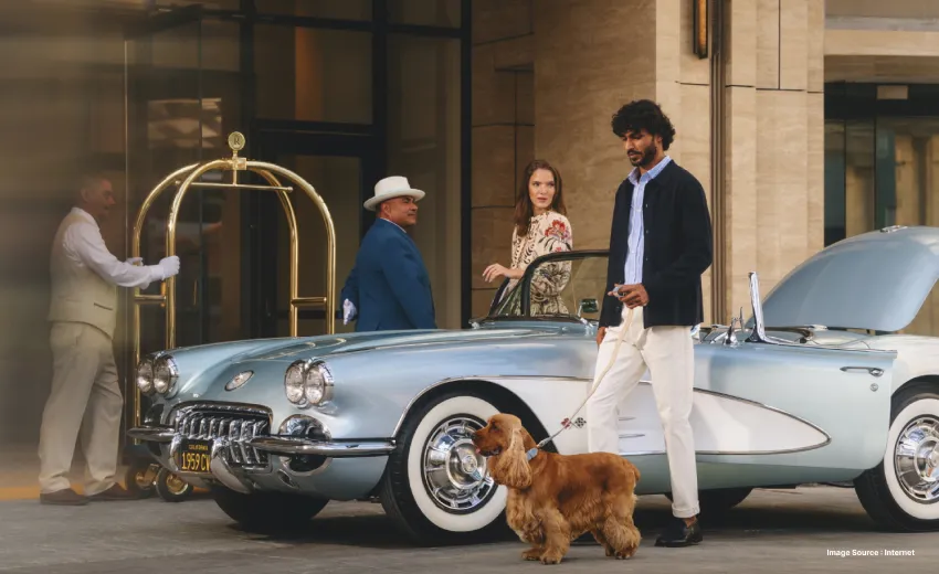 a well dressed tourist walking with his brown dog besides a vintage luxury car