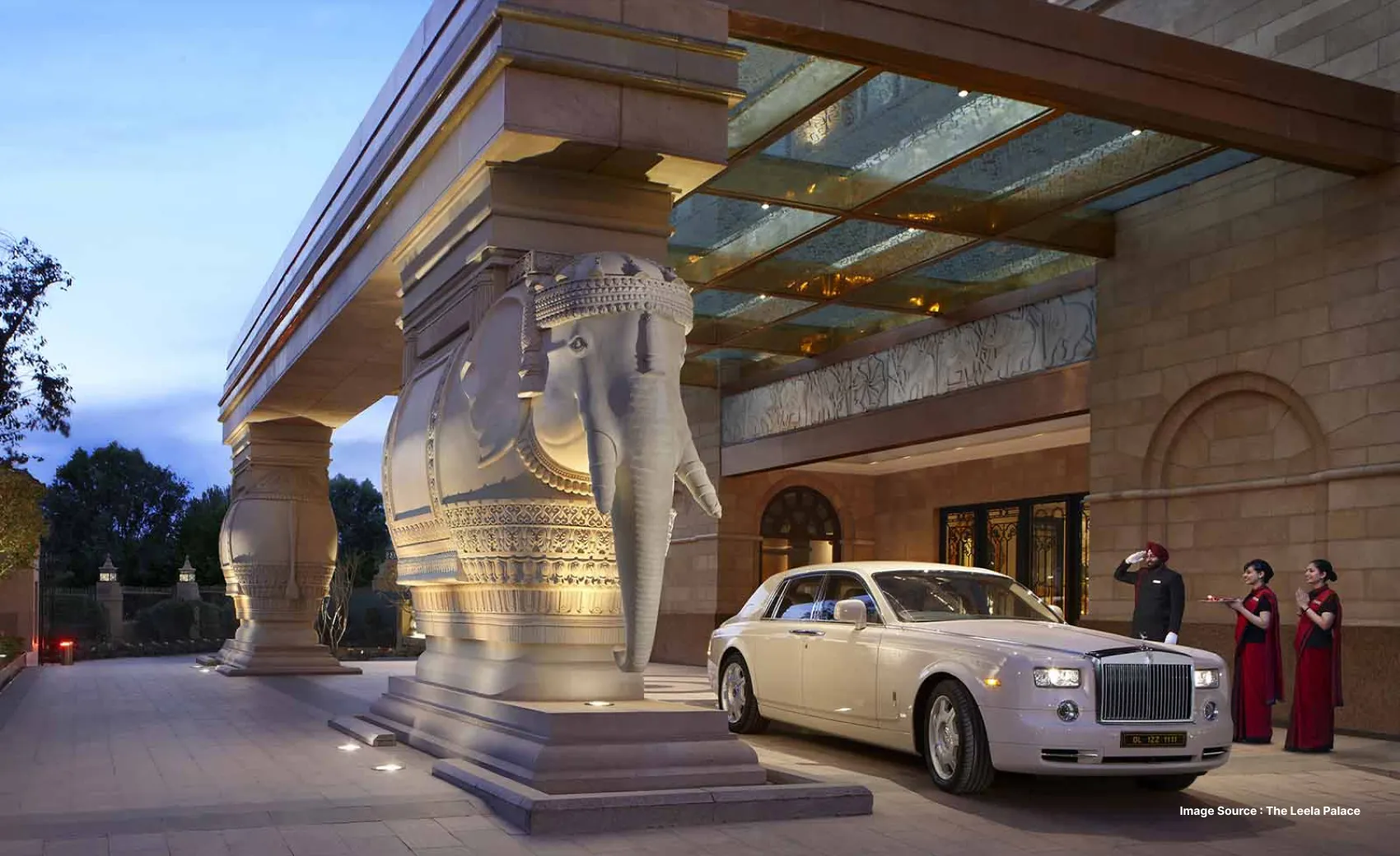 a luxury white vehicle arrives at the entrance of the leela palace in delhi with a unique elephant pillar architecture