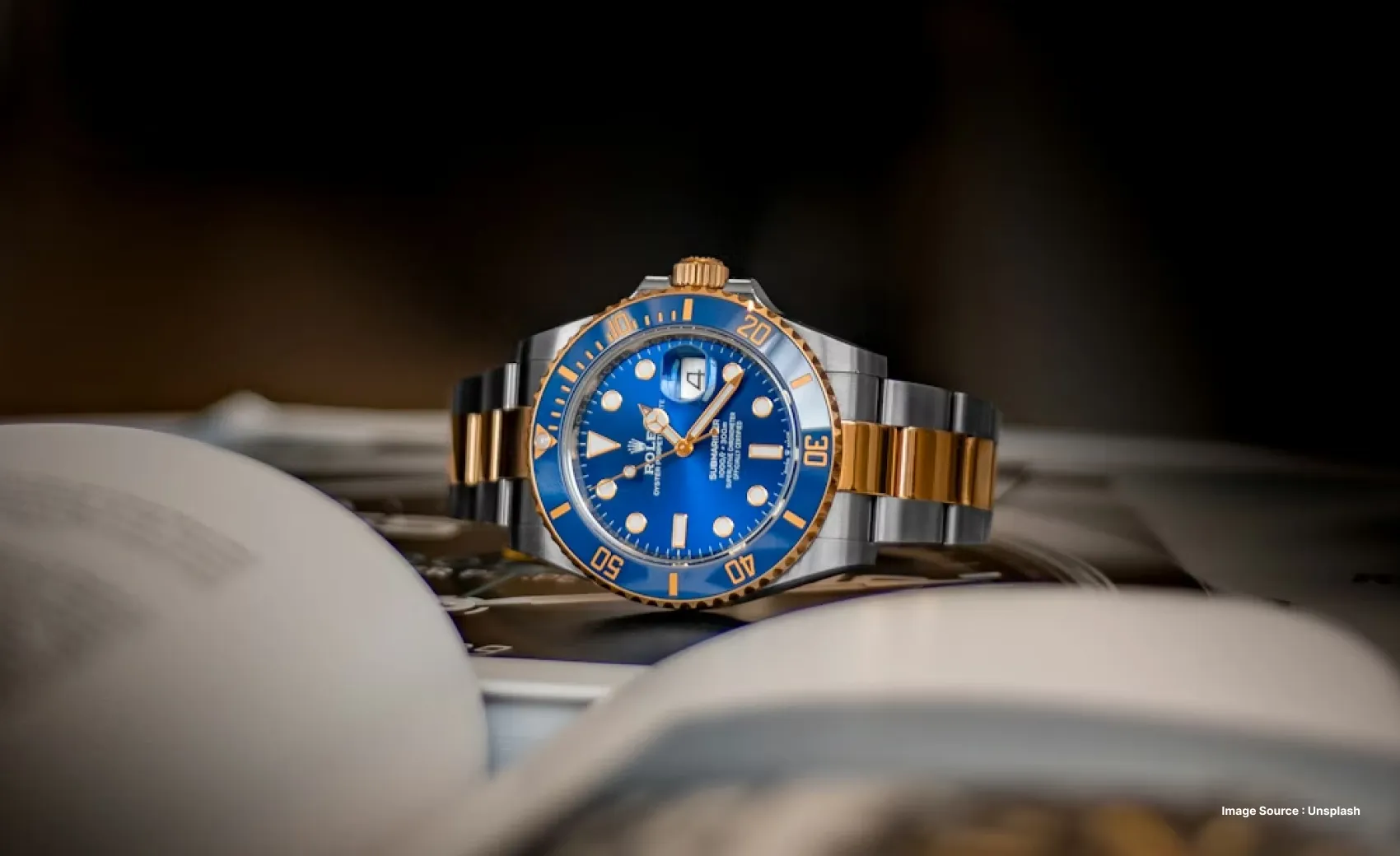 close up a blue rolex watch lying sideways next to a book