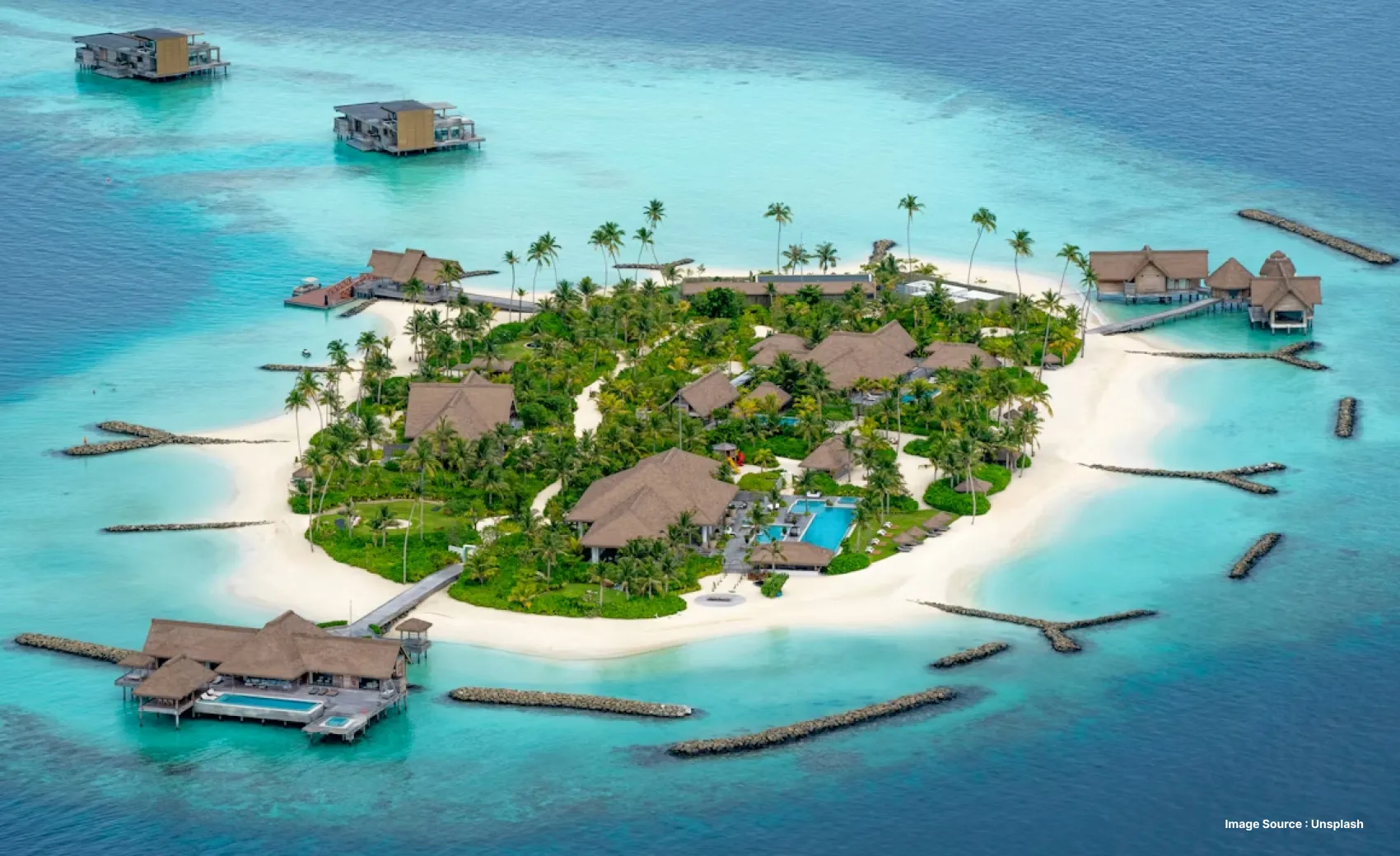aerial shot of an isolated island with palm trees and greenery, and over Water villas in a distance