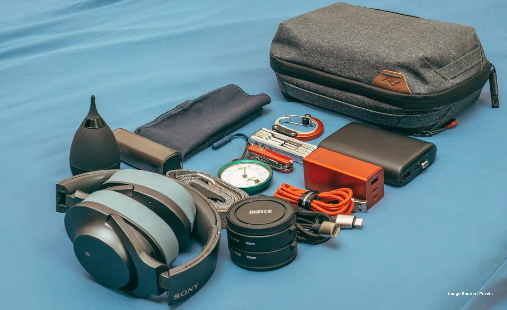 a small grey bag with tech gadgets laid out such as headphones and cables