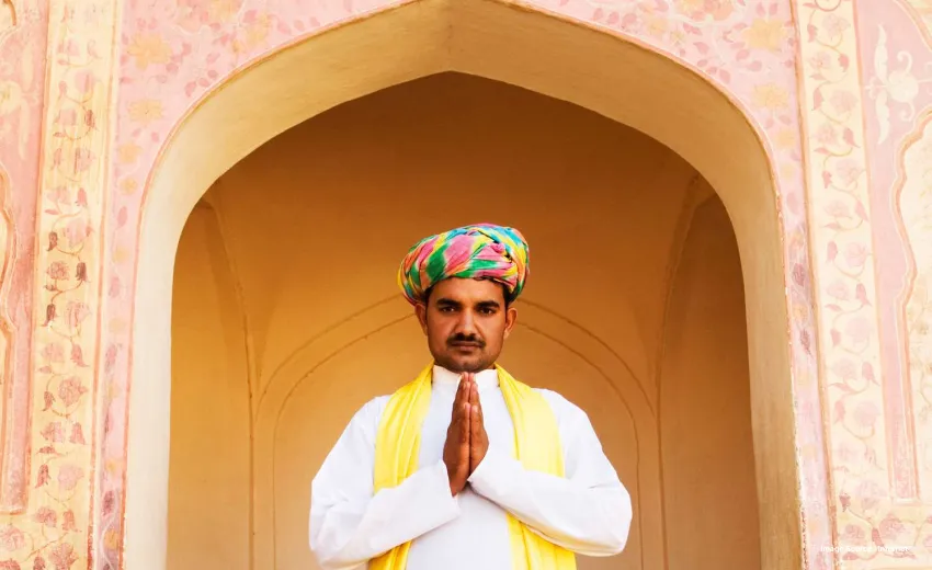 an indian man in a colorful headgear joining his palms together to greet namaste