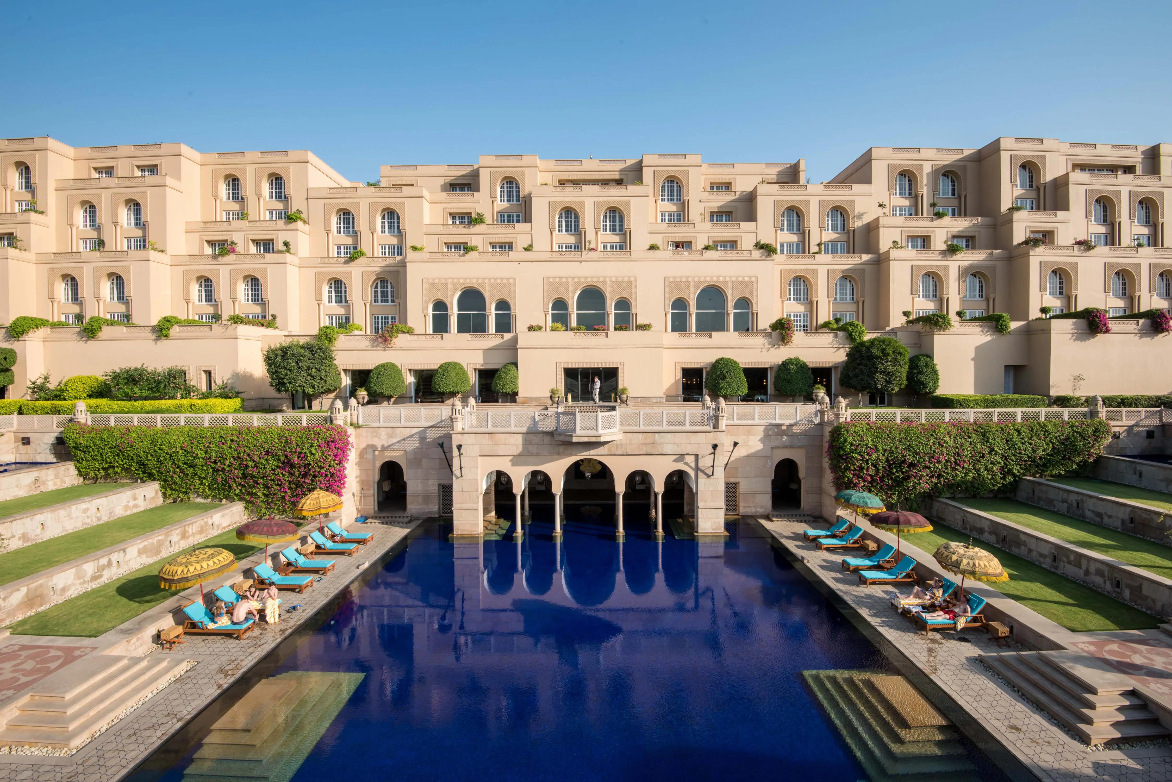 the poolside view of the oberoi amarvilas with mughal inspired archways architecture on a clear sunny day