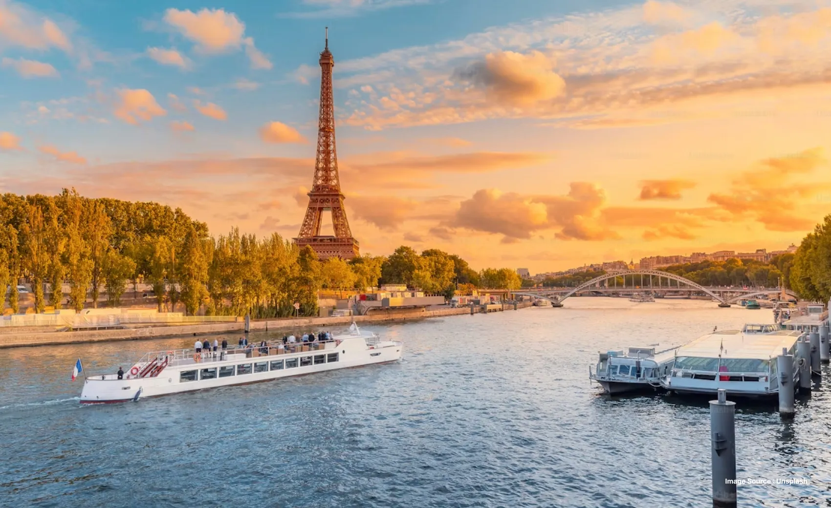 sunset view of the legendary eiffel tower with the river in frame as tourists-filled boats pass by