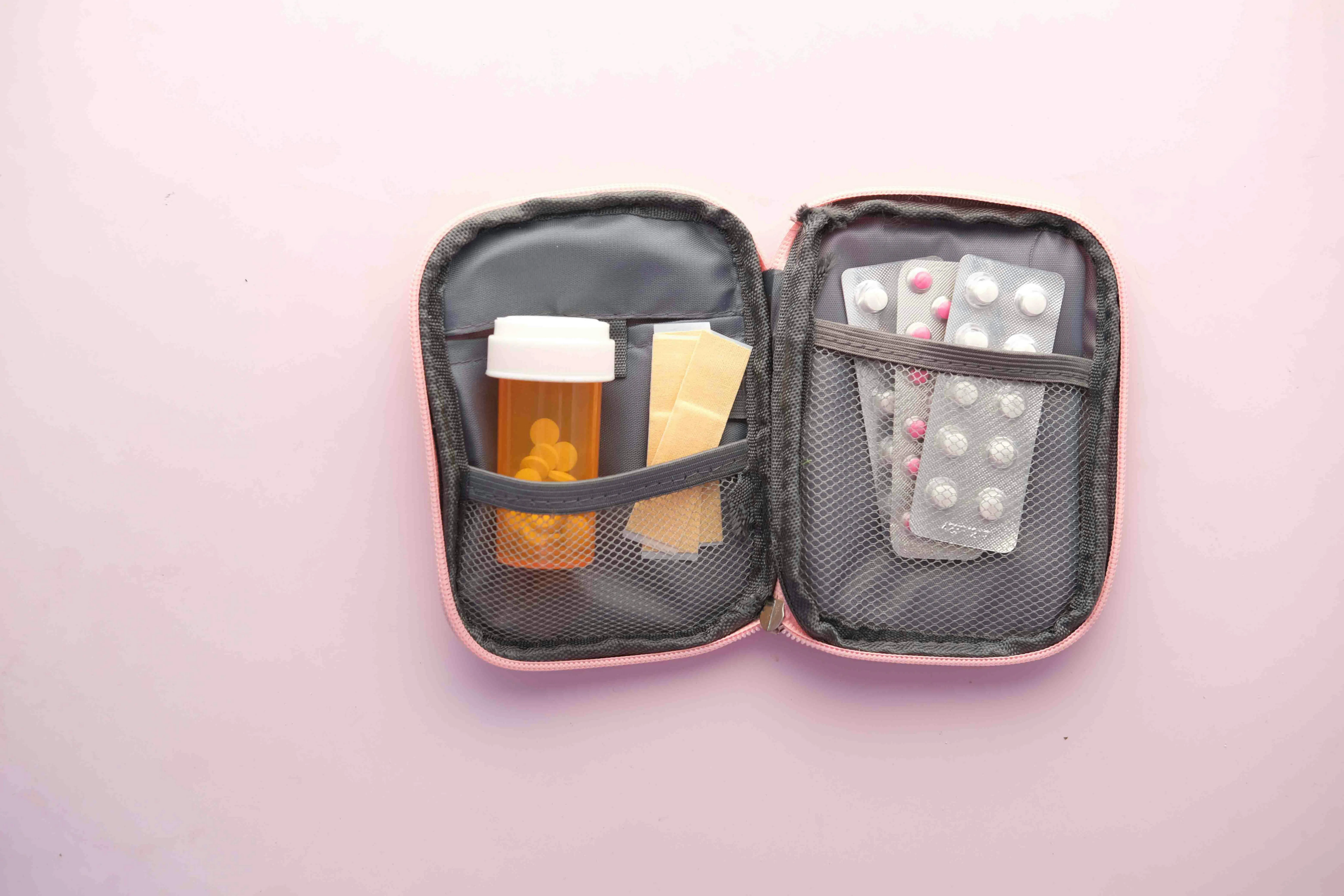 a medicine pouch with medicines and capsules box laid out open on a pink surface