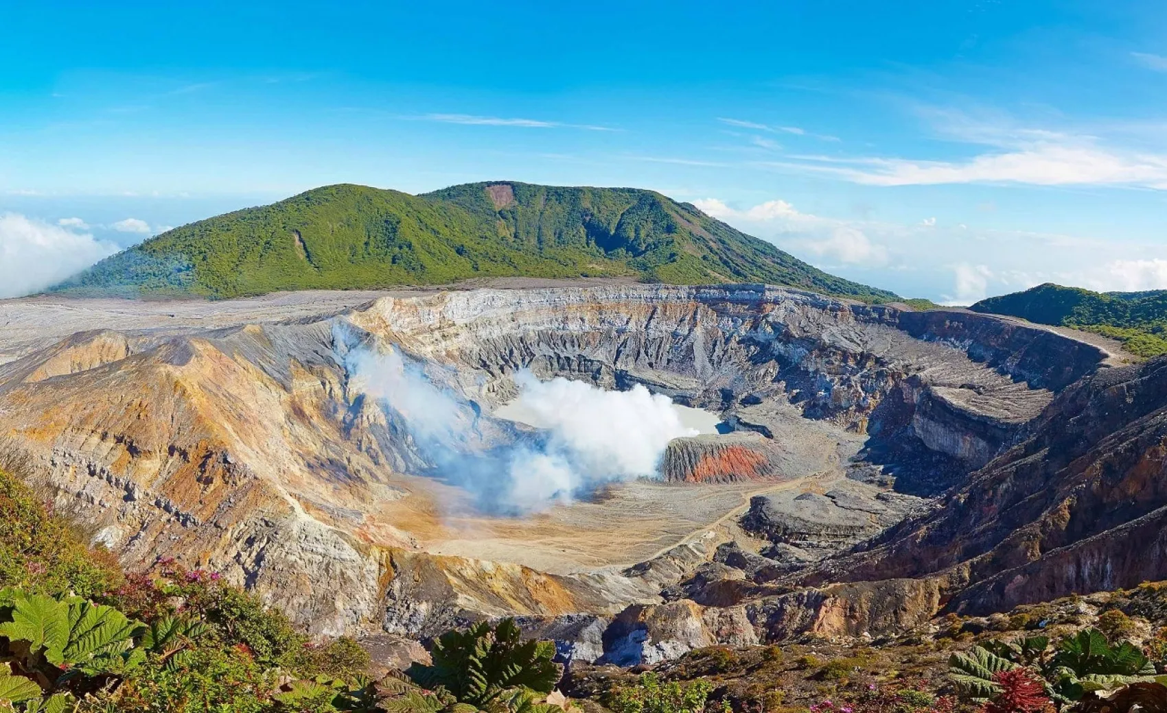 a beautiful view of dense mist rising from a spring in a crater shaped pong with green hill in the background