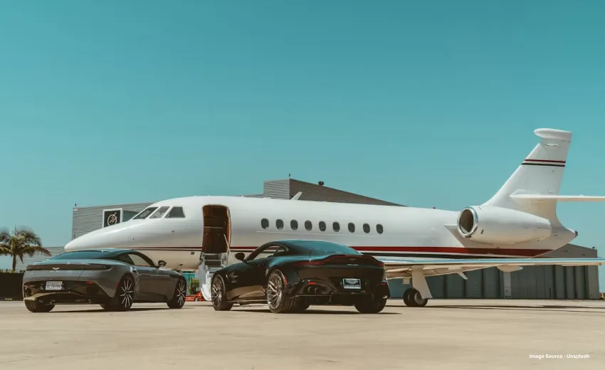 a private jet parked with two black luxury cars in the front during the day