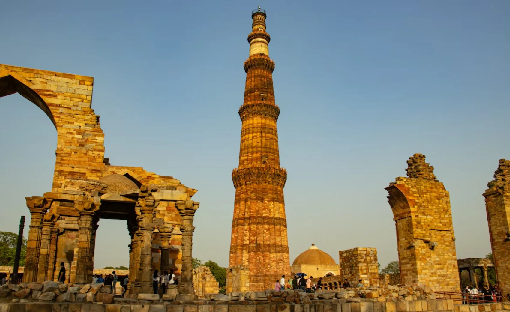 the tall sandstone tower - qutub minar in delhi next to sandstone gate ruins on a clear day
