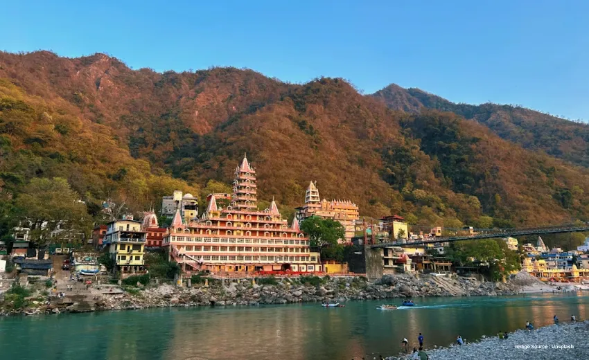 the riverbank view of the Ganges in rishikesh surrounded by small green hills with temples and bridges