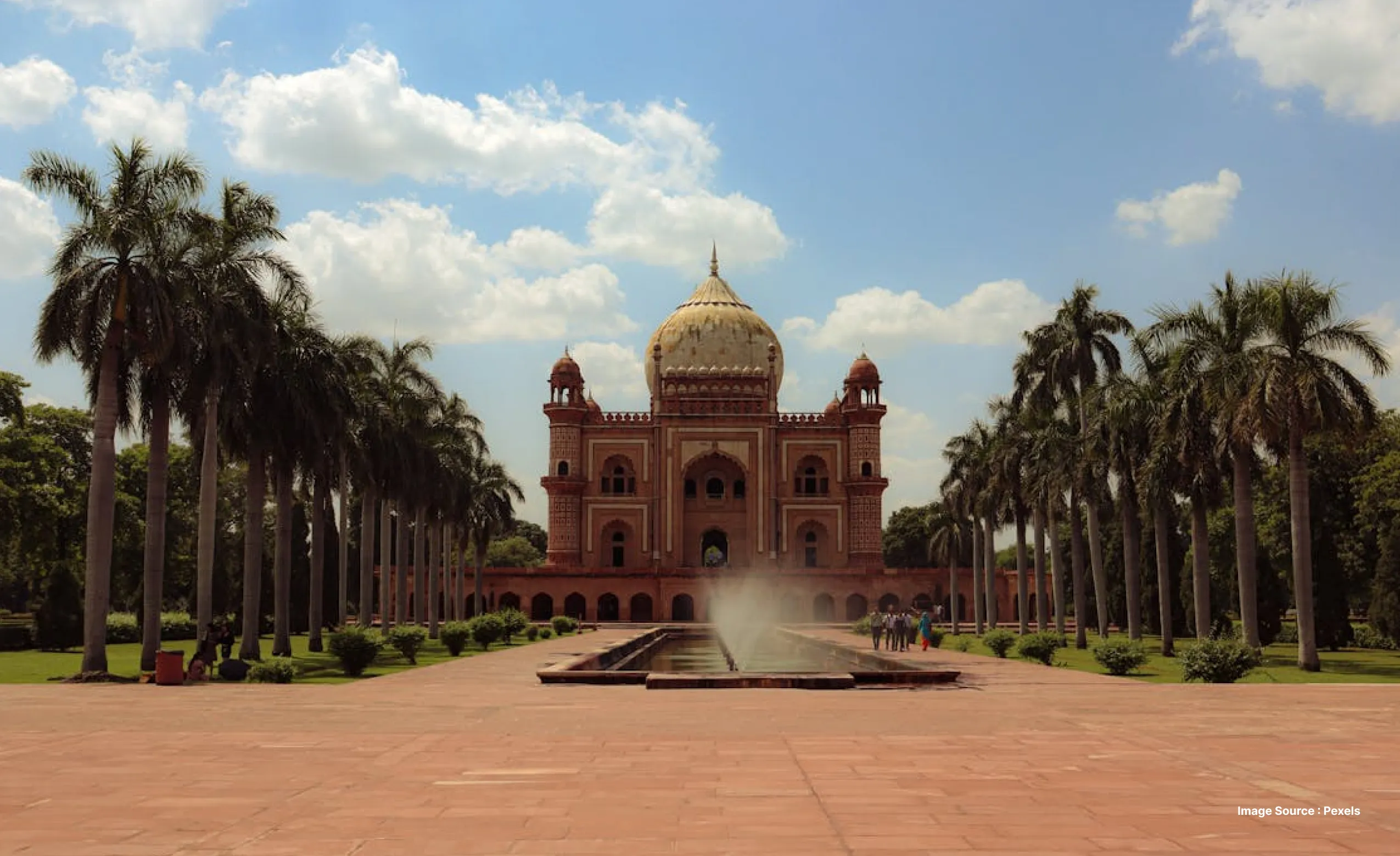 a front side view of the humayun's tomb in delhi, flanked by palm trees on both sides and a fountain lane in the middle