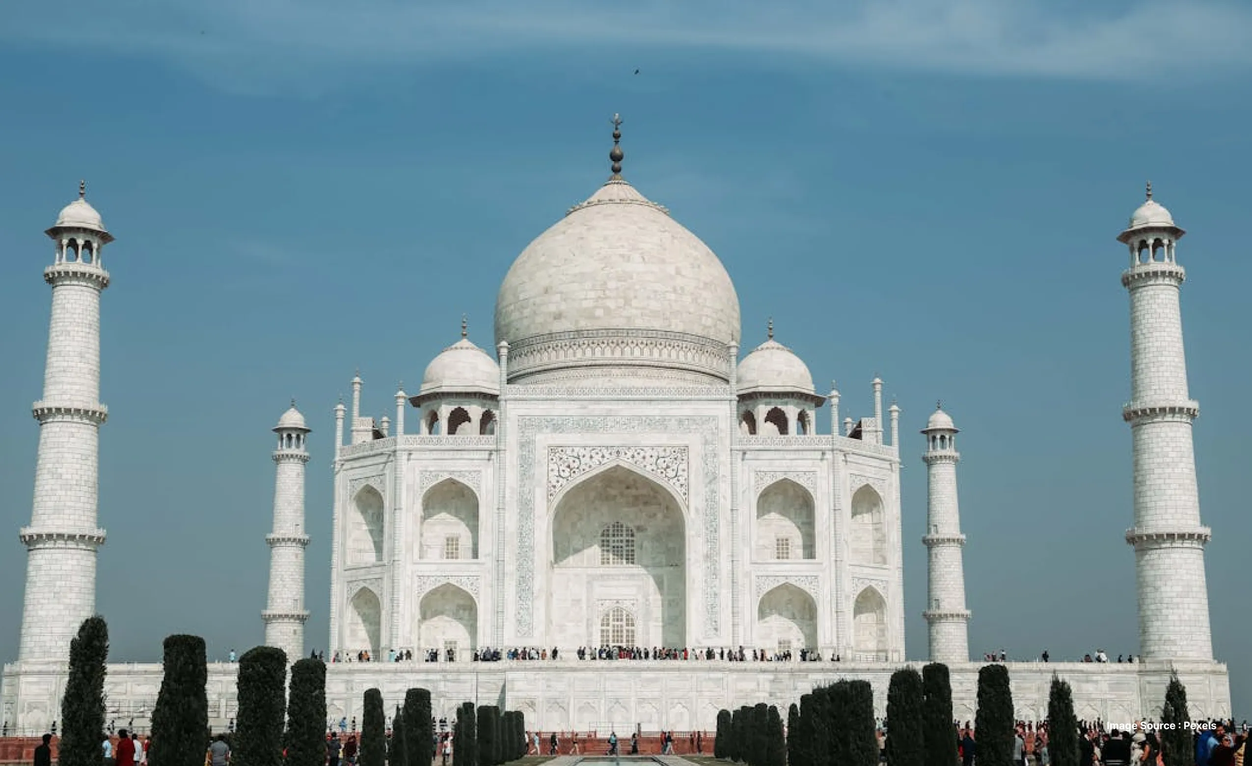a beautiful daytime shot of the iconic taj mahal's marble building with some of the garden's trees visible