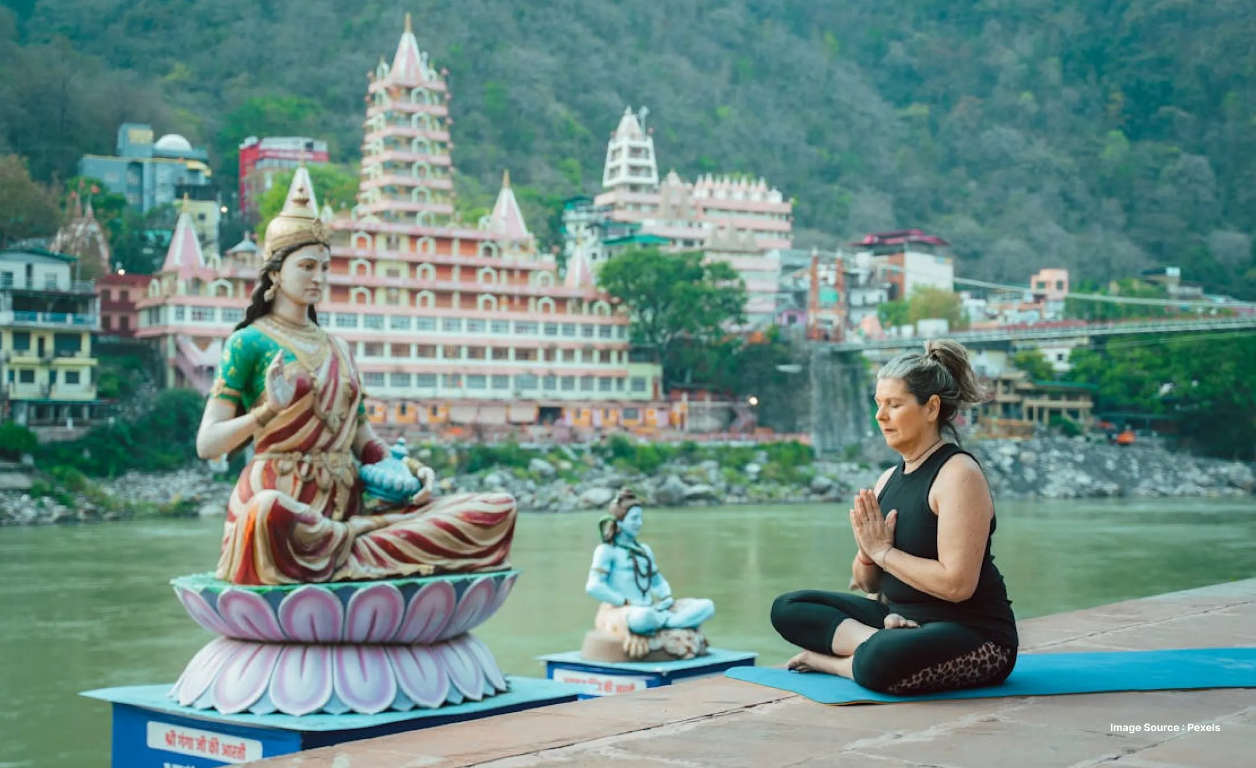 a white woman practices yoga in front of a hindu goddess idol by the side of the ganges river in rishikesh
