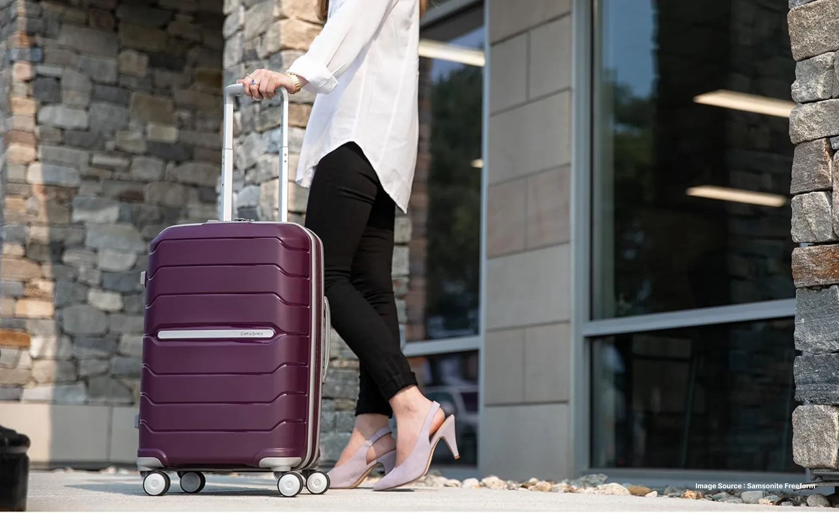 a woman in white shirt and black pants holding the handle of a burgundy hard shell suitcase