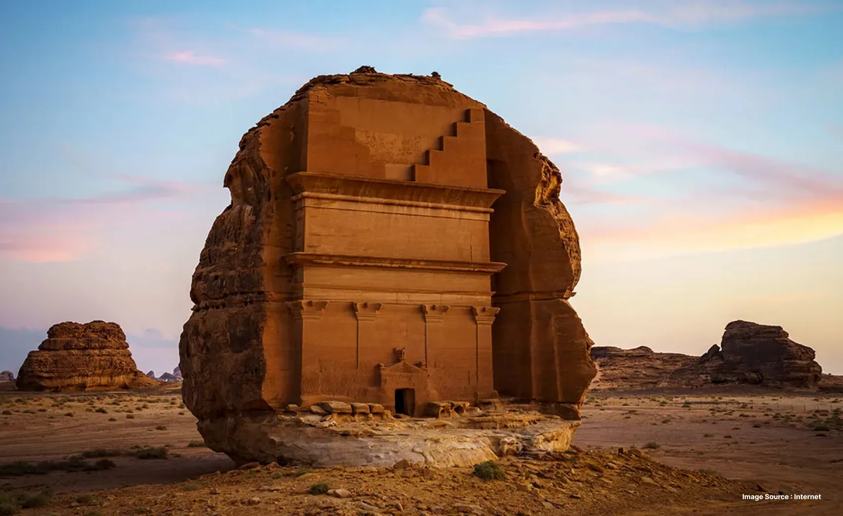 A stand stone structure with a carved door in the middle of a desert landscape during sunset