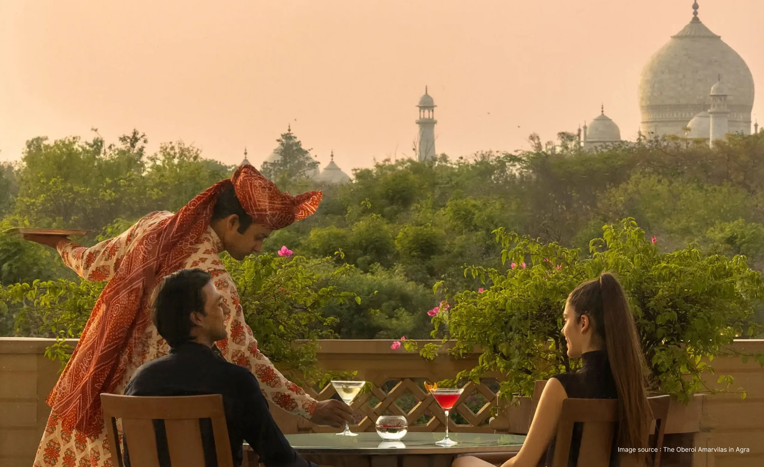a couple enjoying an exclusive dinner as the server puts forward a drink with a view of the taj mahal