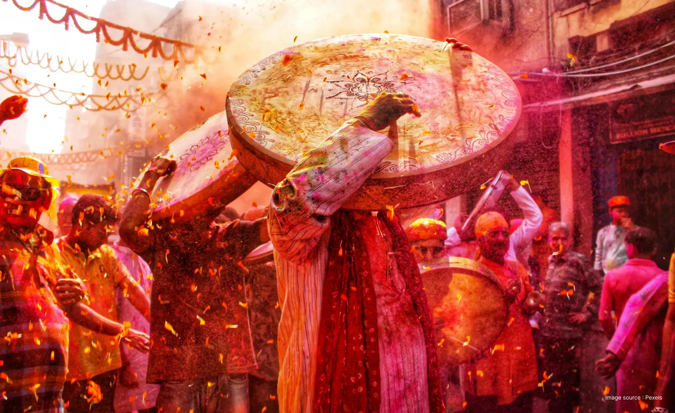 a gorgeous picture of holi celebration in india as a man plays the drum while colors and flowers are thrown in the air