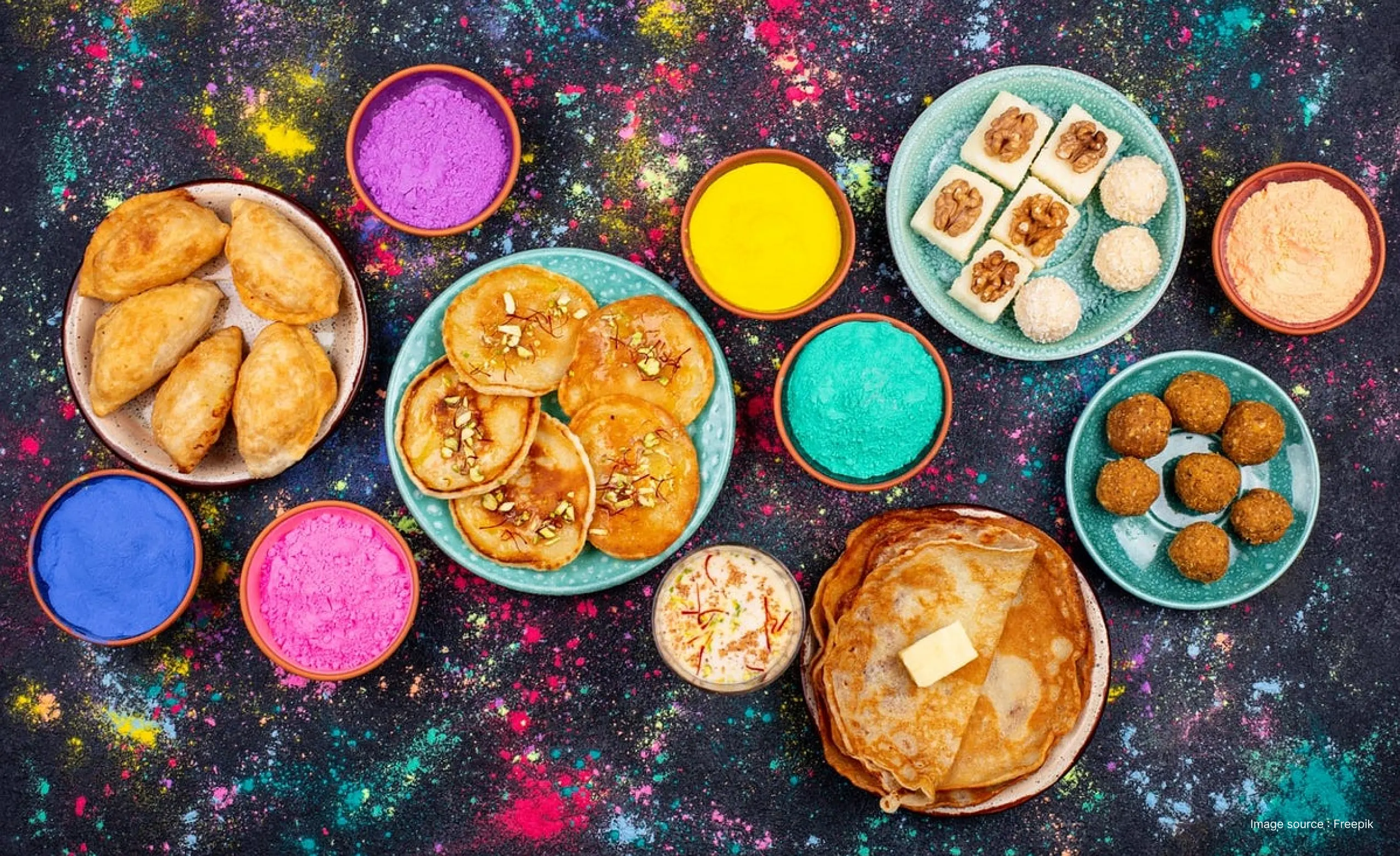 a traditional holi time feast with gujiya, malpua and more on a table with colors spread on it