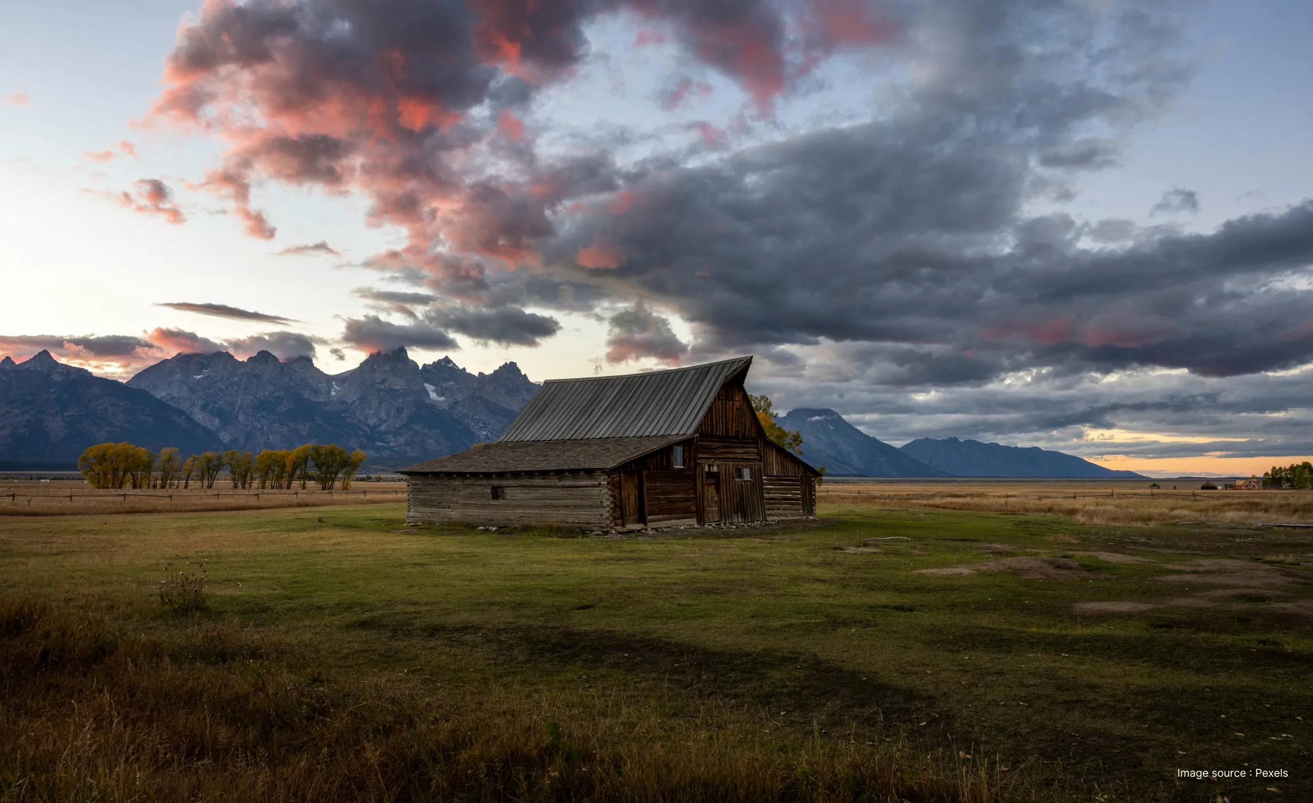 a gorgeous view of the T.A. Moultarn barn with sunset clouds and mountains in the back