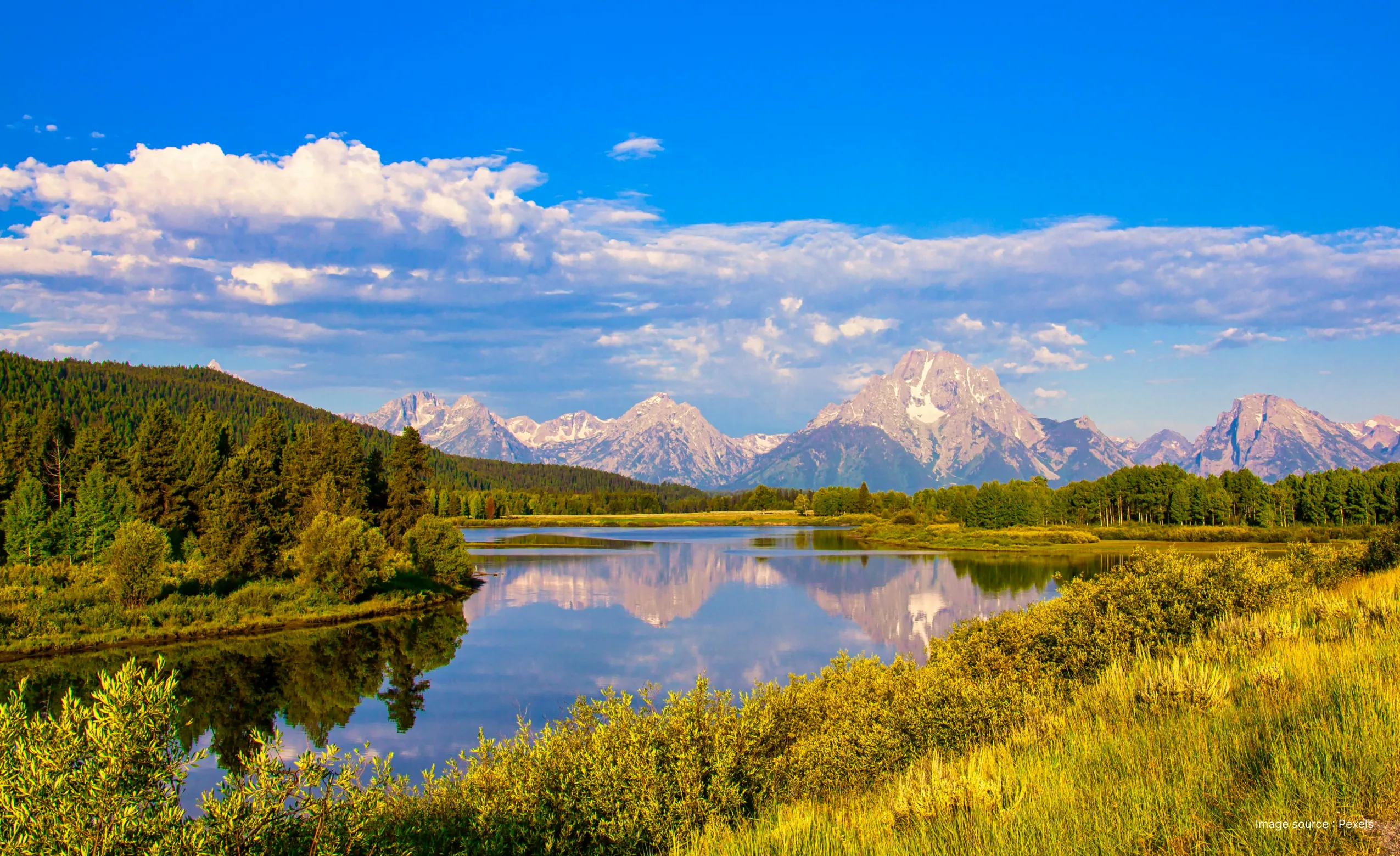a daytime view of the snake river flowing through the lush green plains of the grand tetons