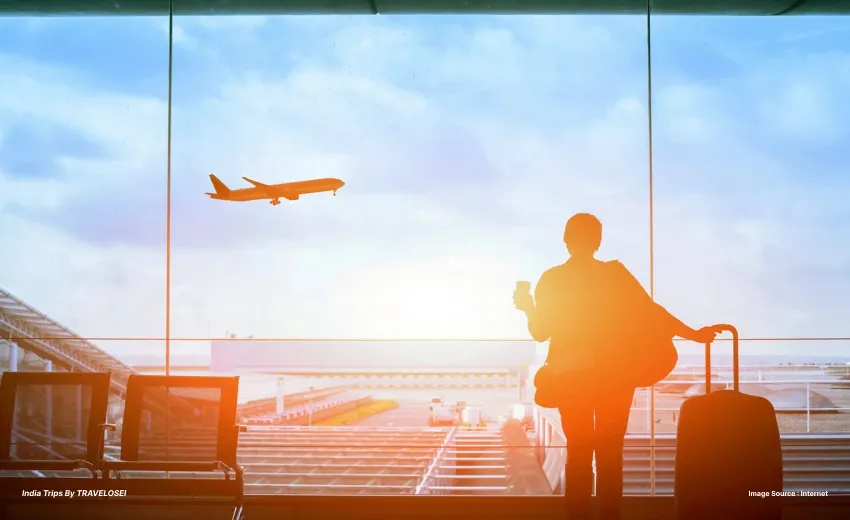 A picture of a woman holding a suitcase at an airport watching an airplane take off.
