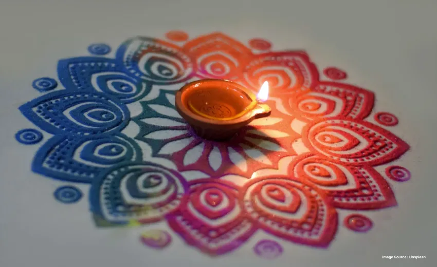 A small diya lit in the centre of a tricoloured rangoli