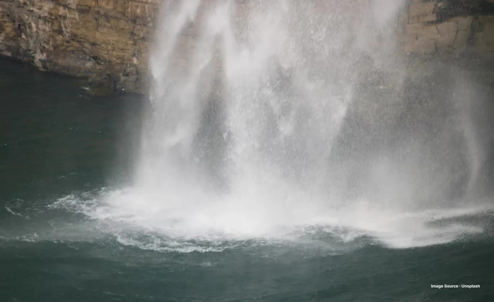 close up of water falling into a waterfall's plunge pool with mist rising from it