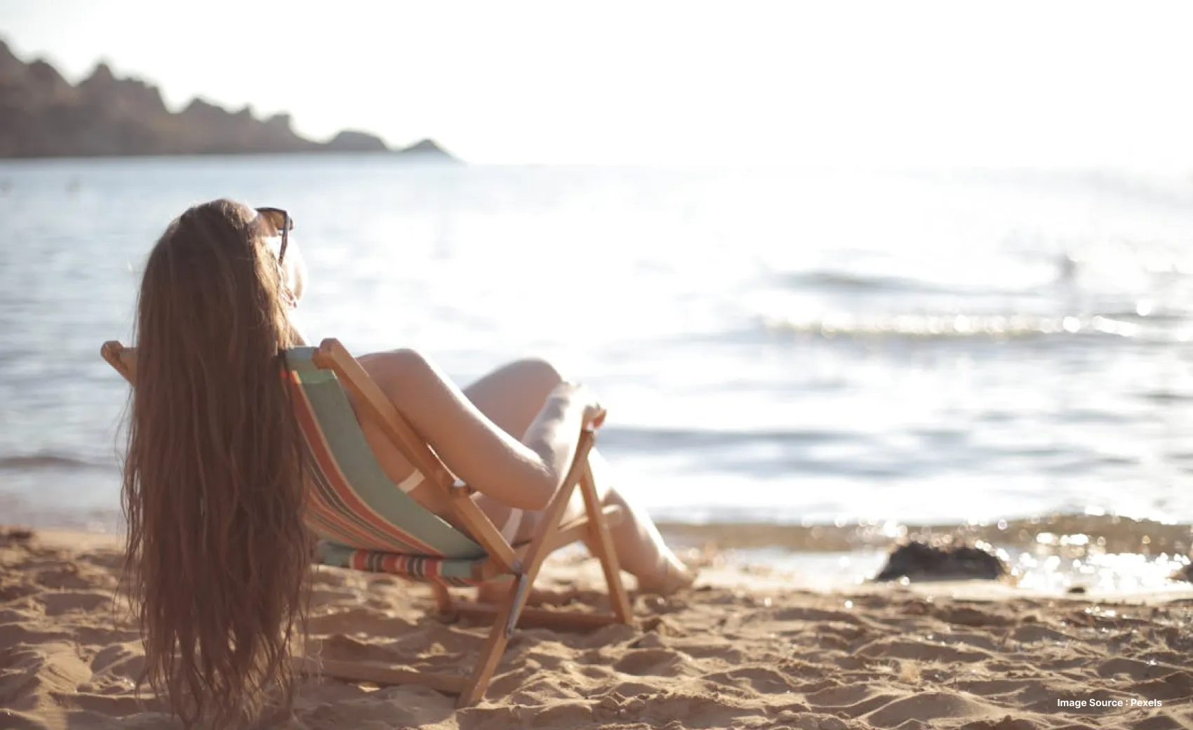 a woman with long hair lounging on a lounge chair at the beach under sun with sunglasses