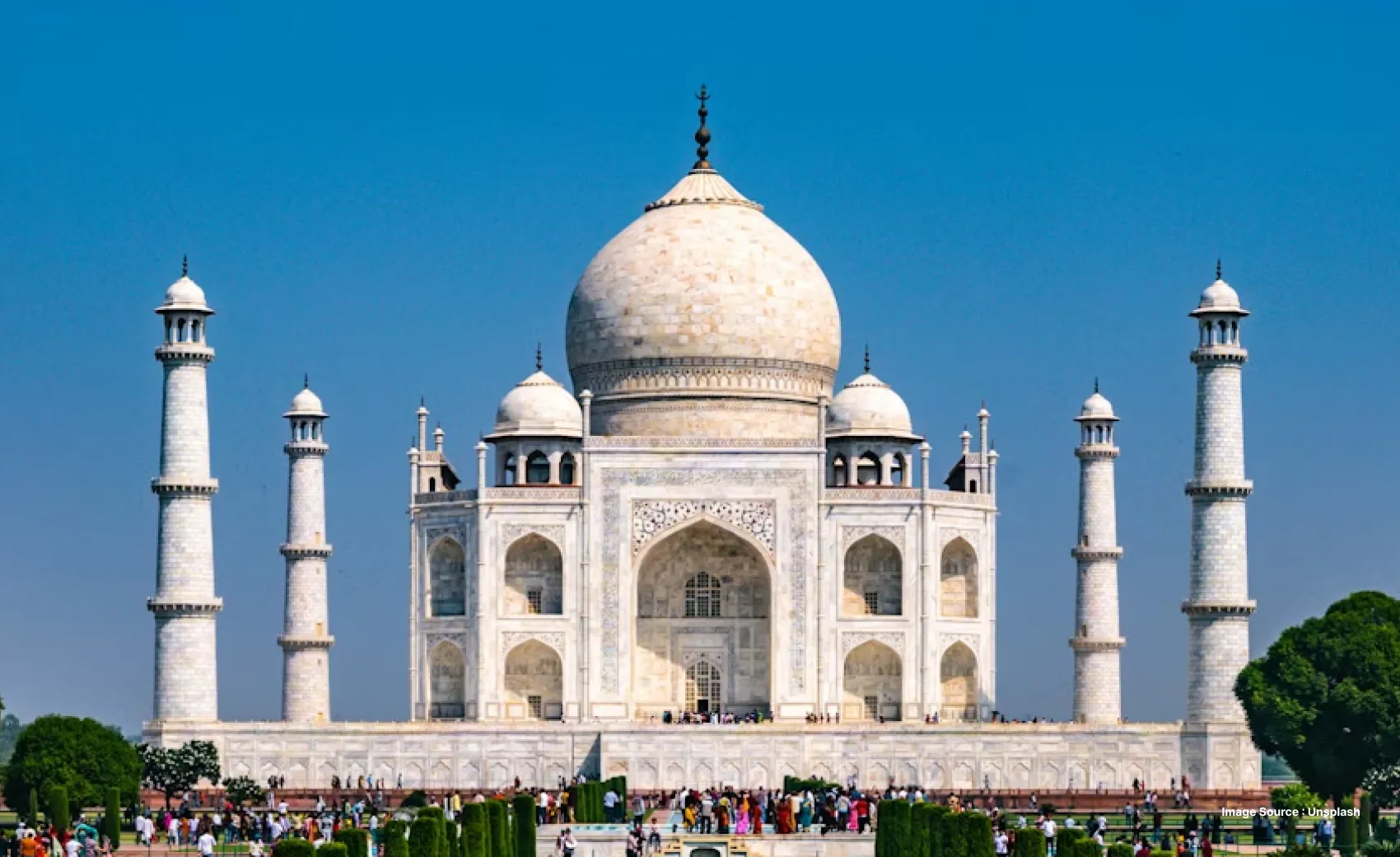 a daytime view of the iconic taj mahal from the front entrance gate with tourists roaming