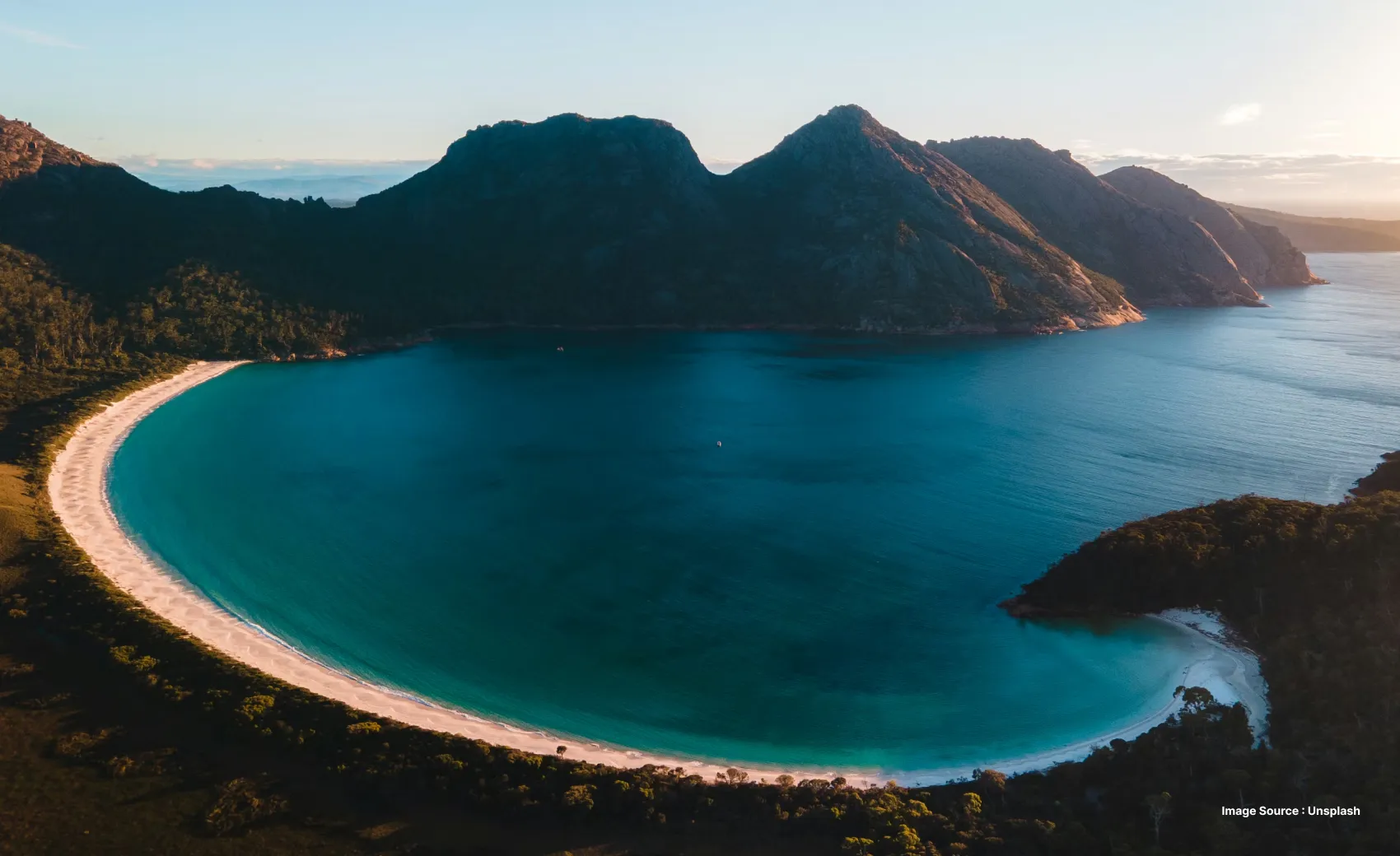 aerial view of tasmania with a clear beach and blue waters surrounded by green hills