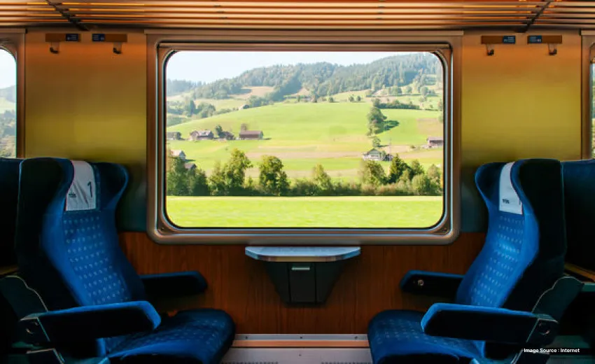 inside of a train with empty blue chairs facing each other and a window showing lush green nature outside