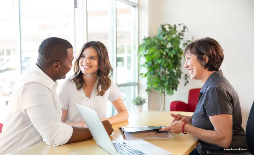 a travel consultant talking happily with a couple dressed in white in a bright room