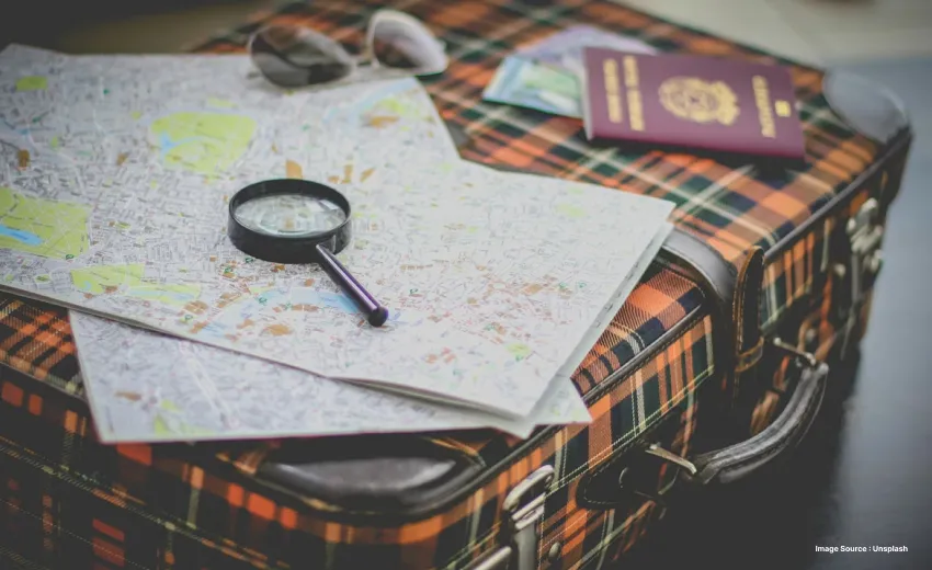 maps lying on a suitcase with sunglasses and a magnifying glass