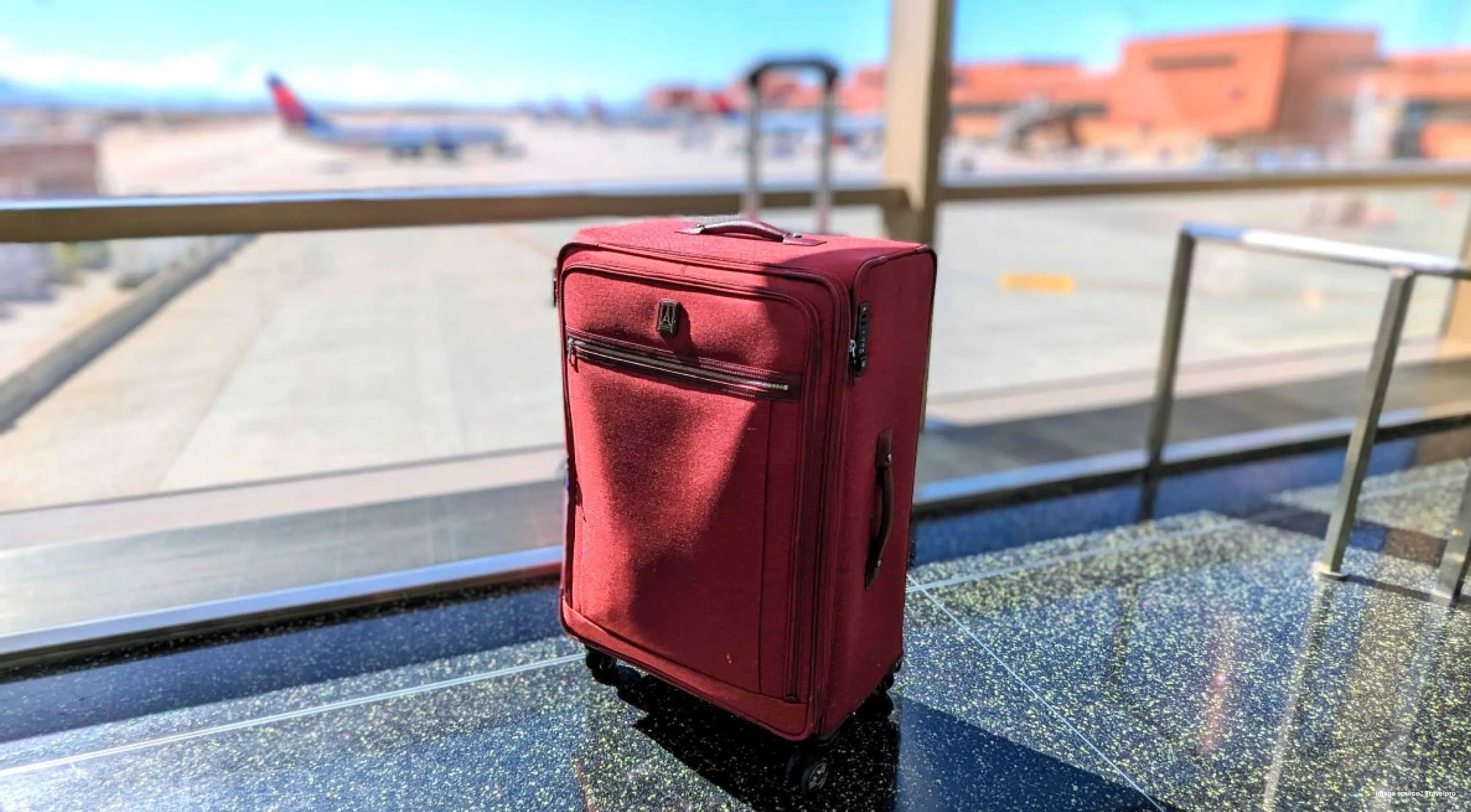 a red suitcase in the airport with a view of the terminal and an airplane