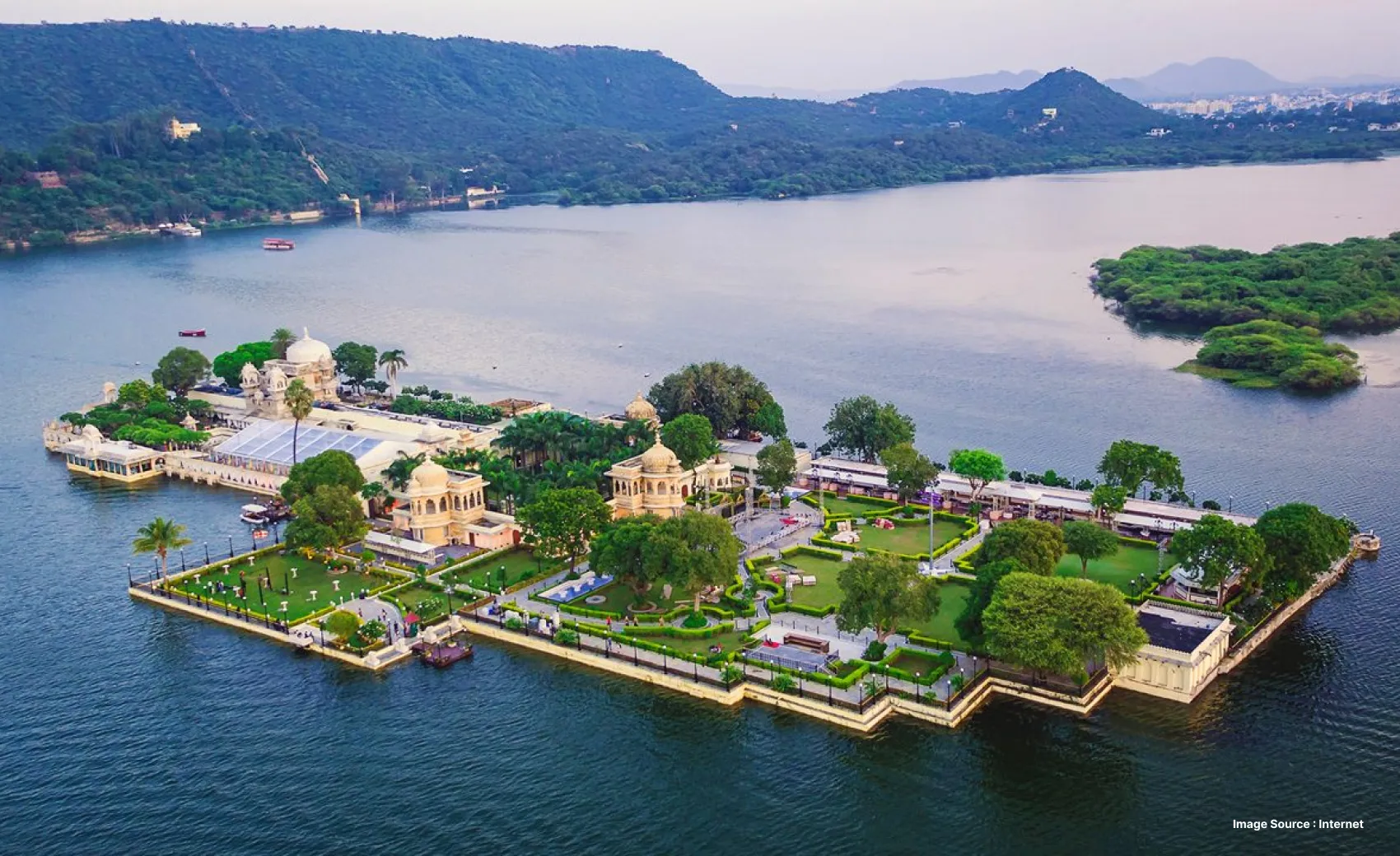 aerial view of a palatial hotel in the middle of the lake in Udaipur with green hills at a distance