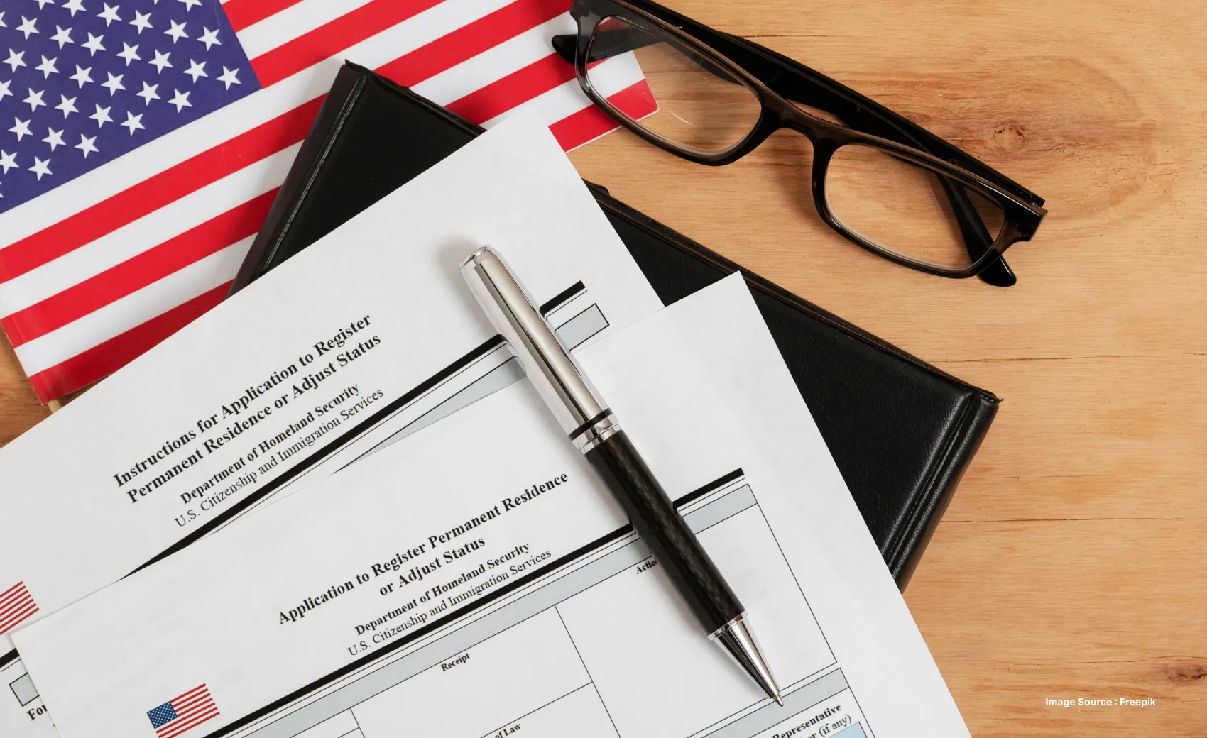 paperwork for usa permanent resident card laid out besides the US flag and a black metal pen on a wooden surface