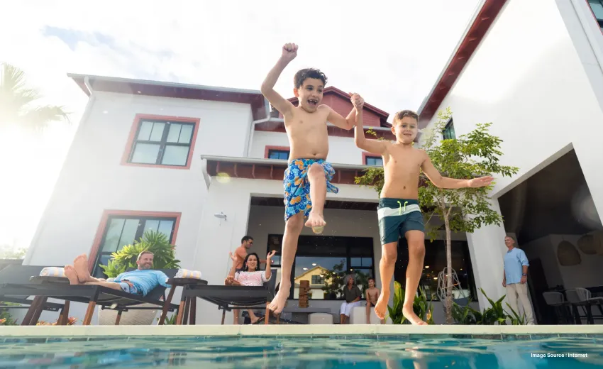 Close up shot of kids jumping into the pool as their family watches them from the lounge chairs in a resort