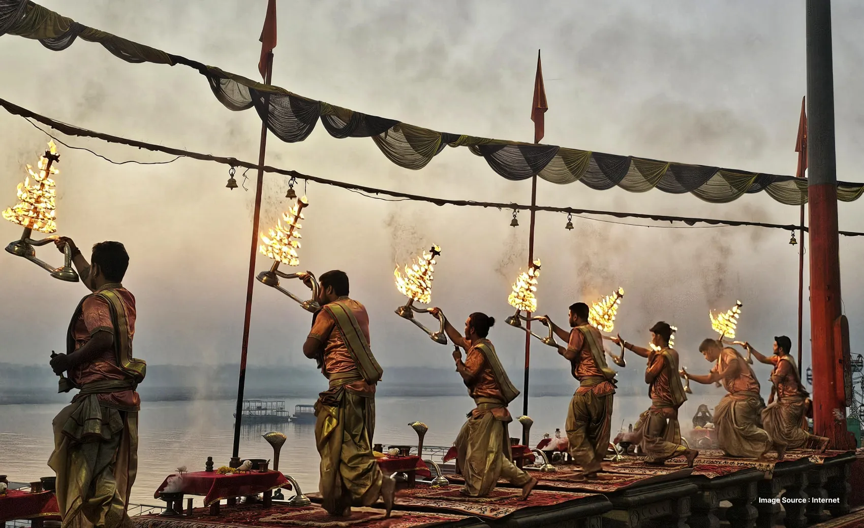 a group of indian priests dressed in orange performing ganga aarti with huge prayer lamps