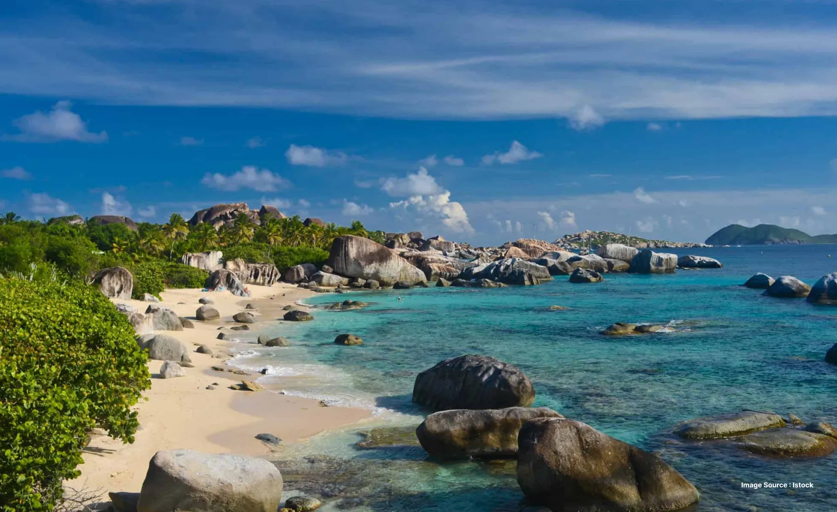 a beach with lots of rounded huge boulders and greenery