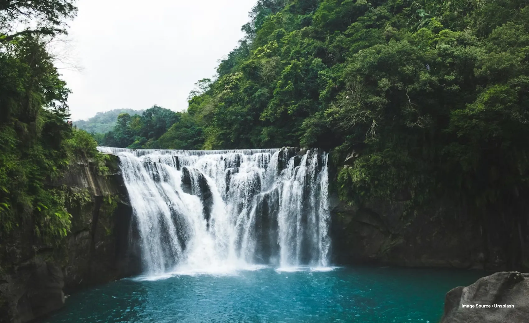 a medium sized waterfall with misty plunge pool surrounded by lush green trees
