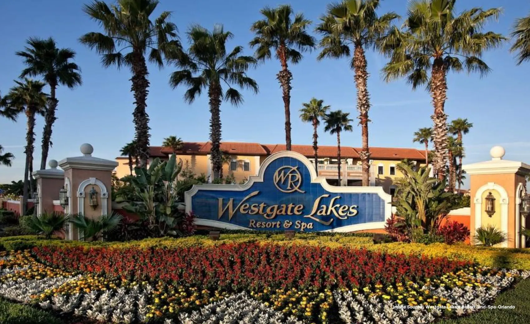 the entrance of westgate lakes resort with a colorful flowerbed and tall palm trees